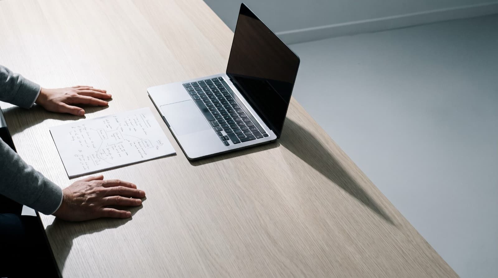 Mains posées sur une table, à côté d'une page annotée à la main et d'un ordinateur portable.