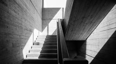 Escalier en béton brut vu en contre-plongée, jeu d'ombre et de lumière rasante sur un coffrage bois, architecture épurée