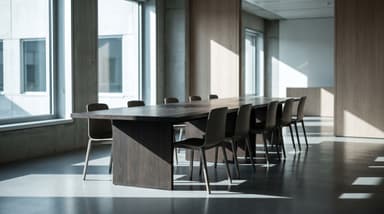 Salle de réunion vide, longue table sombre et chaises inoccupées, grandes baies vitrées, architecture béton et bois.